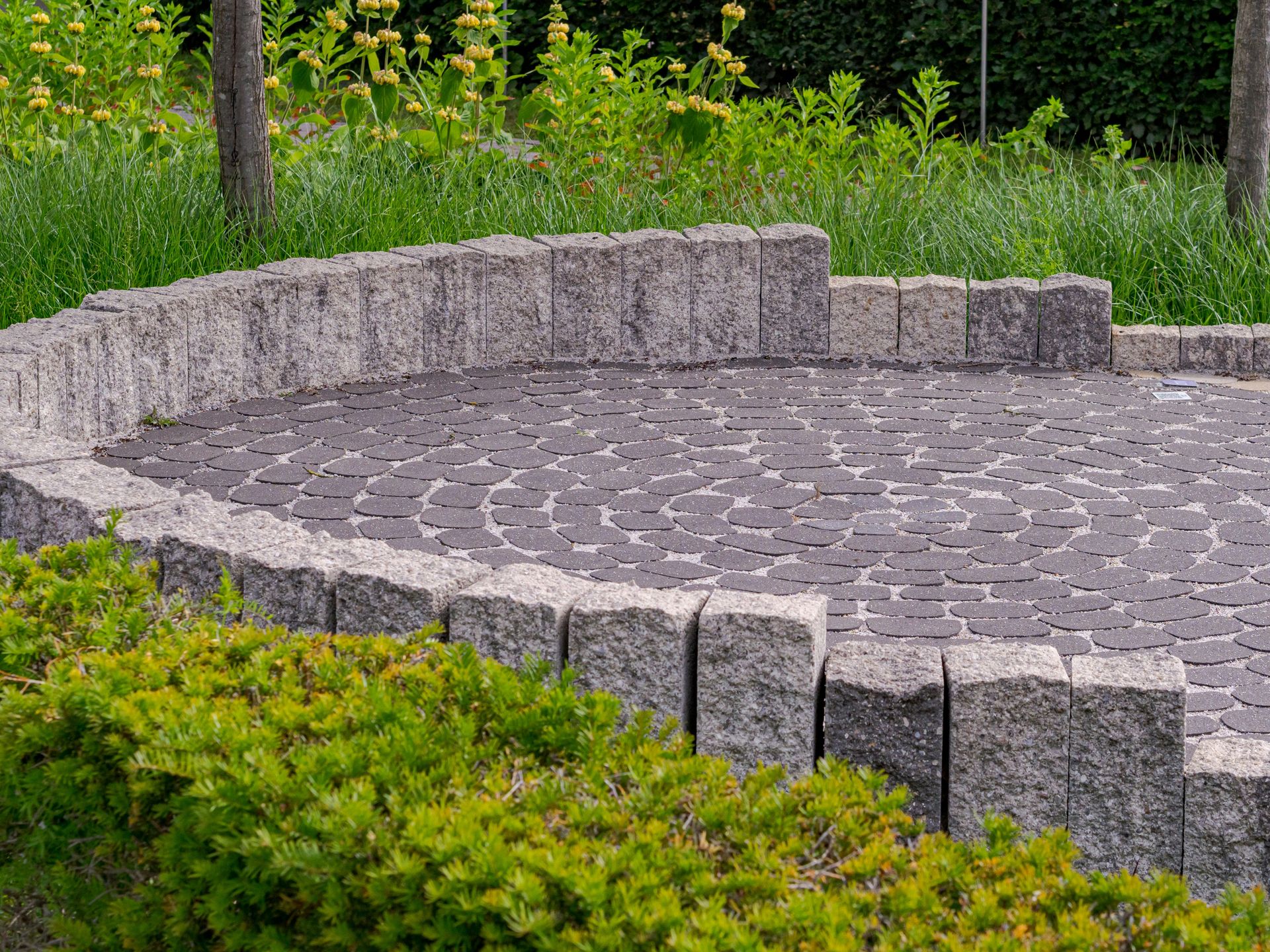 Circular paved patio with low stone wall and green bushes